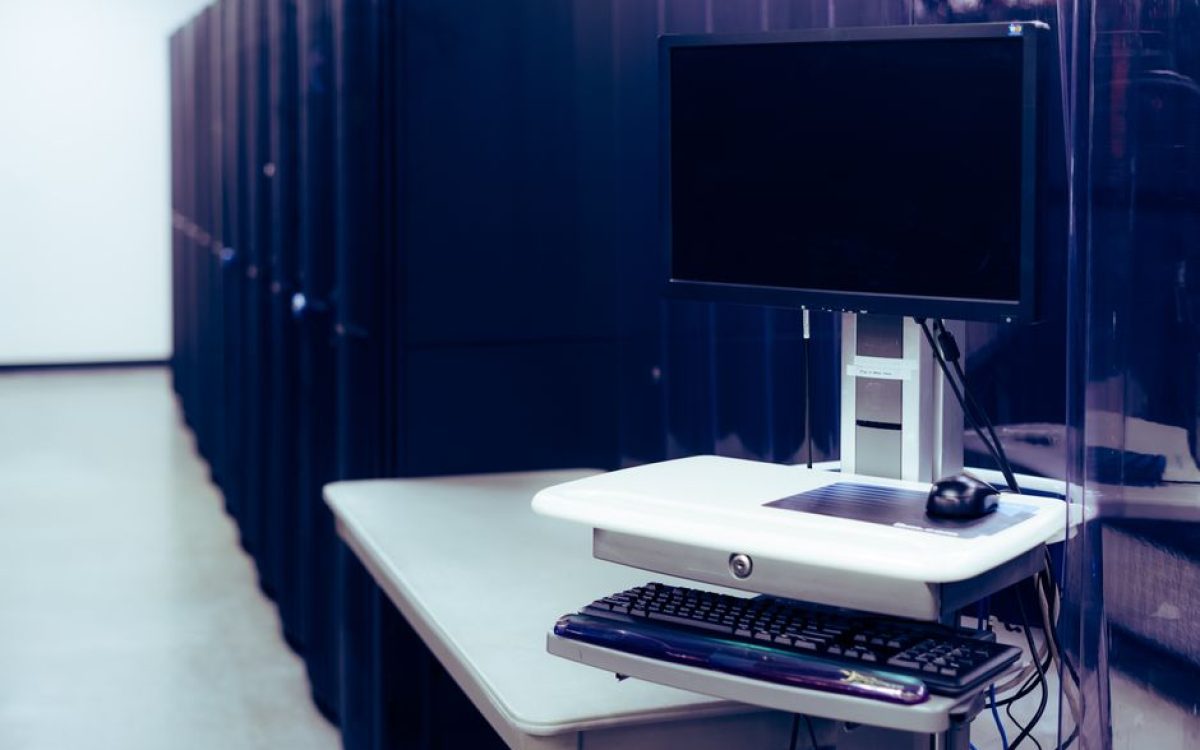 Contemporary computer with black screen placed on stand near row of server steel racks in data center
